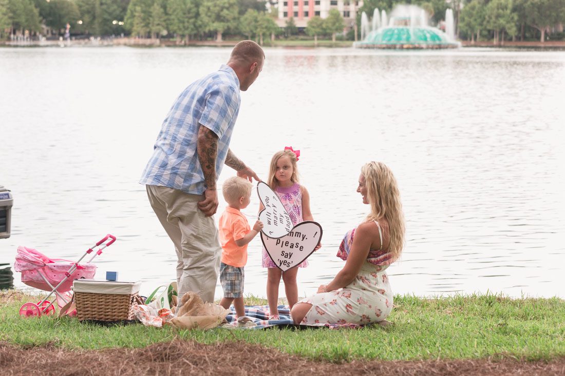 Surprise Orlando proposal photography at Lake Eola park with two kids captured by top Orlando wedding and engagement photographer