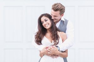 Romantic engagement photo with couple embracing in front of a white wall in historic downtown Winter Garden during their engagement portrait session with top Orlando wedding photographer