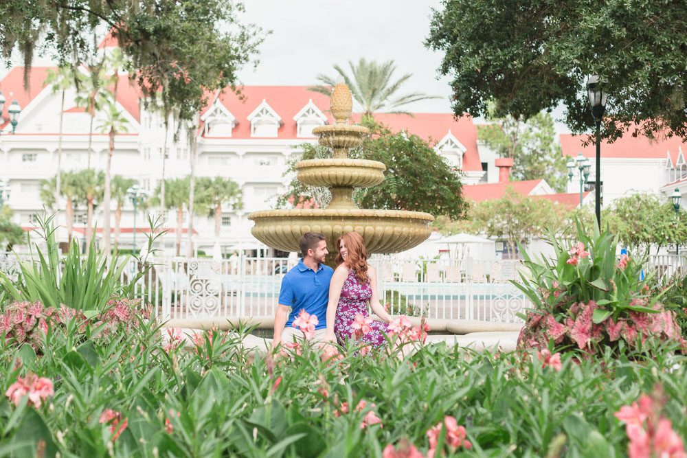 Newly engaged couple poses in front of a fountain at Disney's Grand Floridian Resort amongst flowers during their Orlando engagement photography session