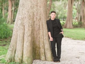 Beautiful bride poses in black suit against a tree at Kraft Azalea intimate garden wedding