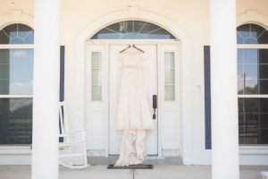 Brides wedding dress hanging in a doorway for a rustic chic country wedding at a barn captured by Orlando wedding photographer and videographer