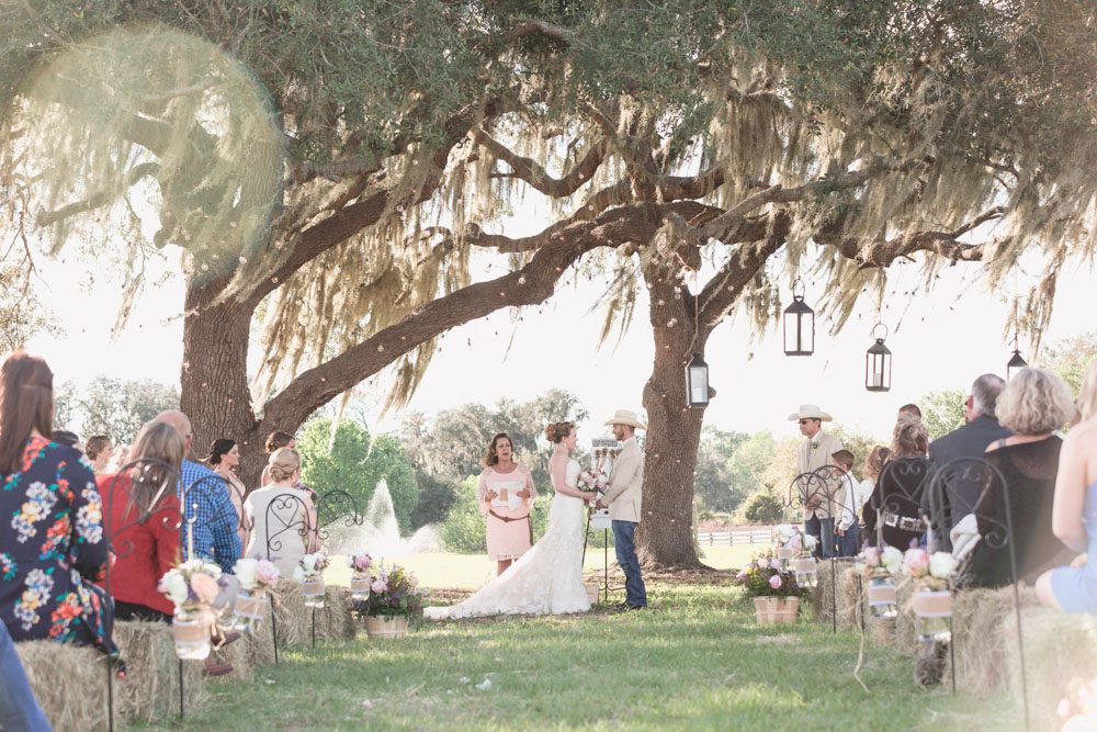 Beautiful outdoor wedding ceremony under a tree with guests sitting on hay bales for a country inspired wedding day in Central Florida