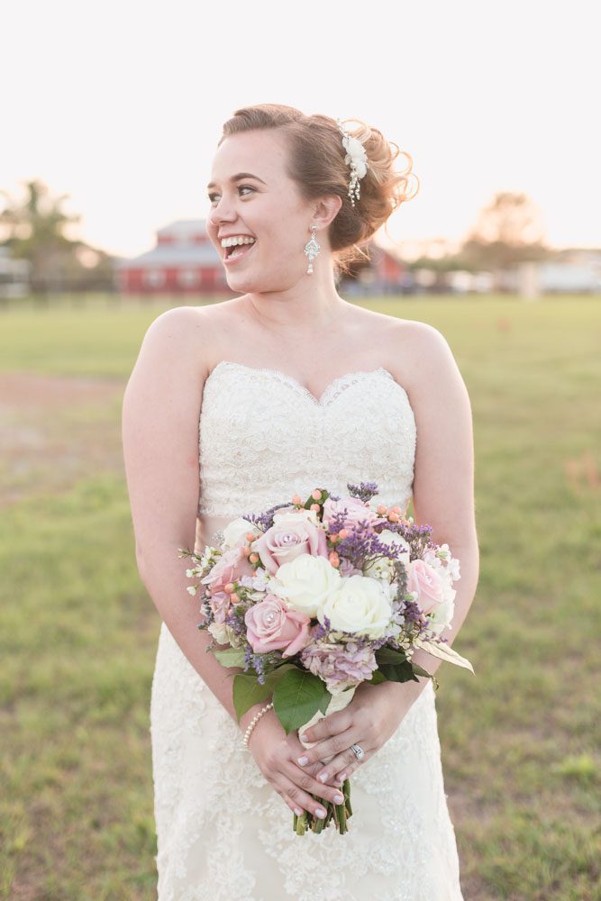 Bride wearing a lace dress and holding a purple and pink bouquet for her country rustic wedding day at a barn north of Orlando