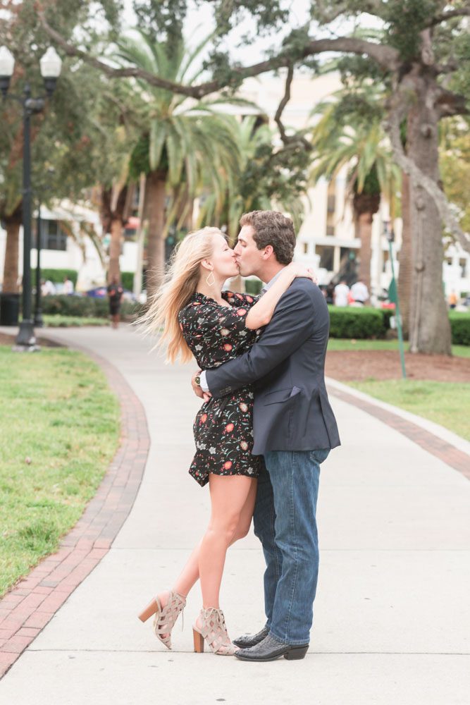 Newly engaged couple kisses along the sidewalk at Lake Eola in downtown Orlando after their surprise proposal is captured by top Orlando photography team