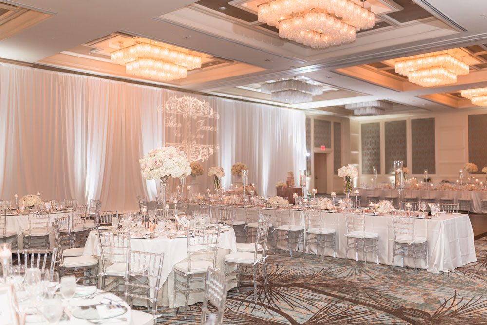 Reception ballroom for a Four Seasons wedding day featuring clear chairs and white, ivory and blush pink decor in Orlando