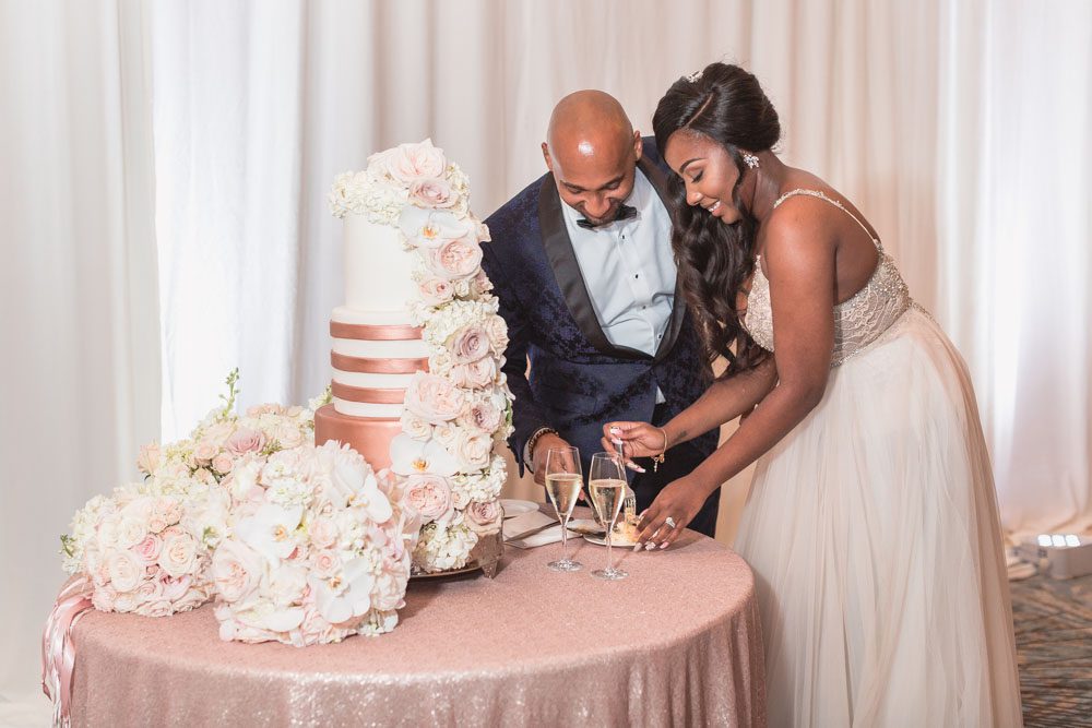Orlando wedding photographer captures couple cutting of gold and white wedding cake with flowers at the Four Seasons