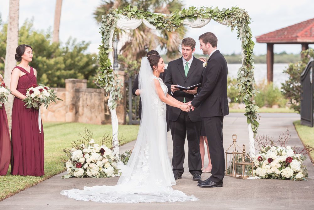 Outdoor wedding ceremony under a greenery arch at the Estate on the Halifax in Port Orange captured by Orlando wedding photographer