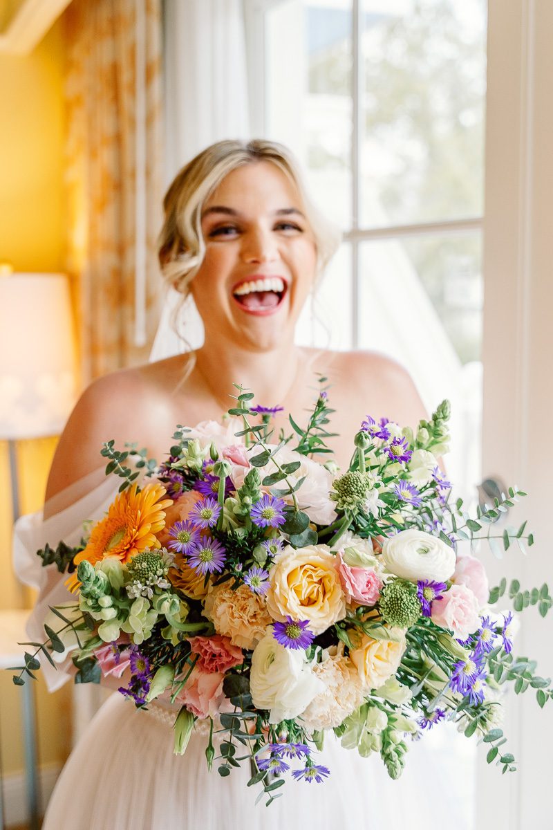 Fun image of bride laughing while holding a vibrant colorful spring bouquet for Disney wedding at the Boardwalk Inn