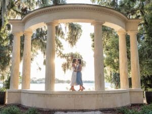 LGBTQ couple standing close together under the iconic columned monument at Kraft Azalea Park in taken by top Orlando wedding photographer, with golden sunlight
