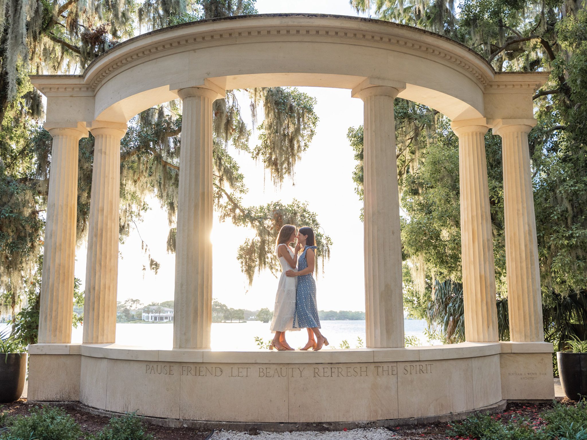LGBTQ couple standing close together under the iconic columned monument at Kraft Azalea Park in taken by top Orlando wedding photographer, with golden sunlight 