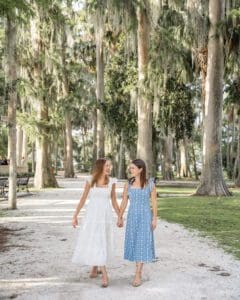 Happy couple in sundresses walking hand in hand on a park trail. Engagement session by Orlando Top Wedding Photographer