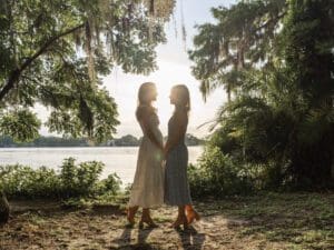 LGBTQ couple standing close together with golden sunlight streaming through the trees. Top Orlando Photo&Video