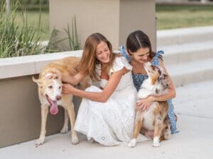 Joyful LGBTQ engagement photo featuring a couple sitting with their two dogs on a park walkway in Kraft Azalea by Orlando Wedding Photographer