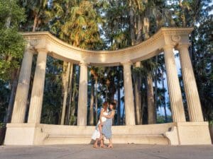 LGBTQ couple standing close together under the iconic columned monument at Kraft Azalea Park in taken by top Orlando wedding photographer, with golden sunlight
