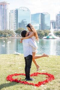 Lake Eola surprise proposal photographed by an Orlando proposal photographer with a heart of fresh red rose petals overlooking the water.