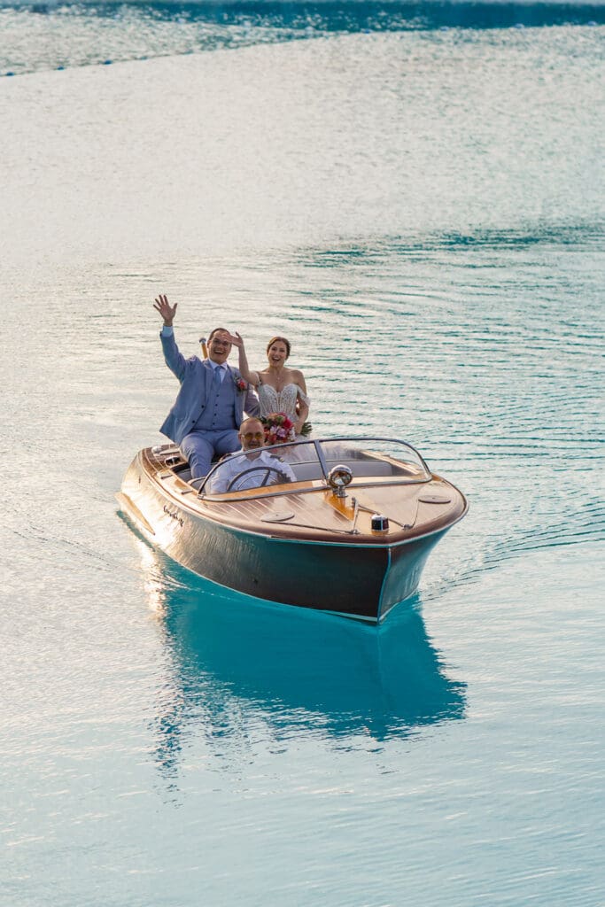 Newlyweds wave goodbye during their unforgettable boat exit at Evermore Resort in Orlando, Captured by Elle, premier wedding photographer & videographer