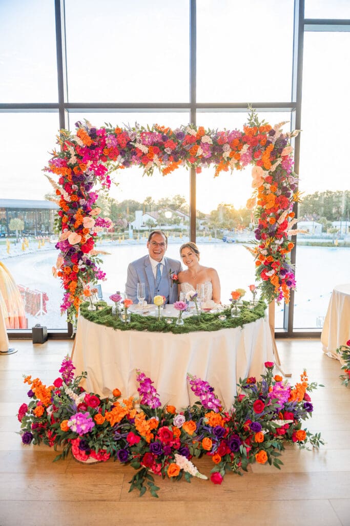 Colorful floral designs frame the sweetheart table at this breathtaking Evermore Resort wedding in Orlando, photographed by Captured by Elle.